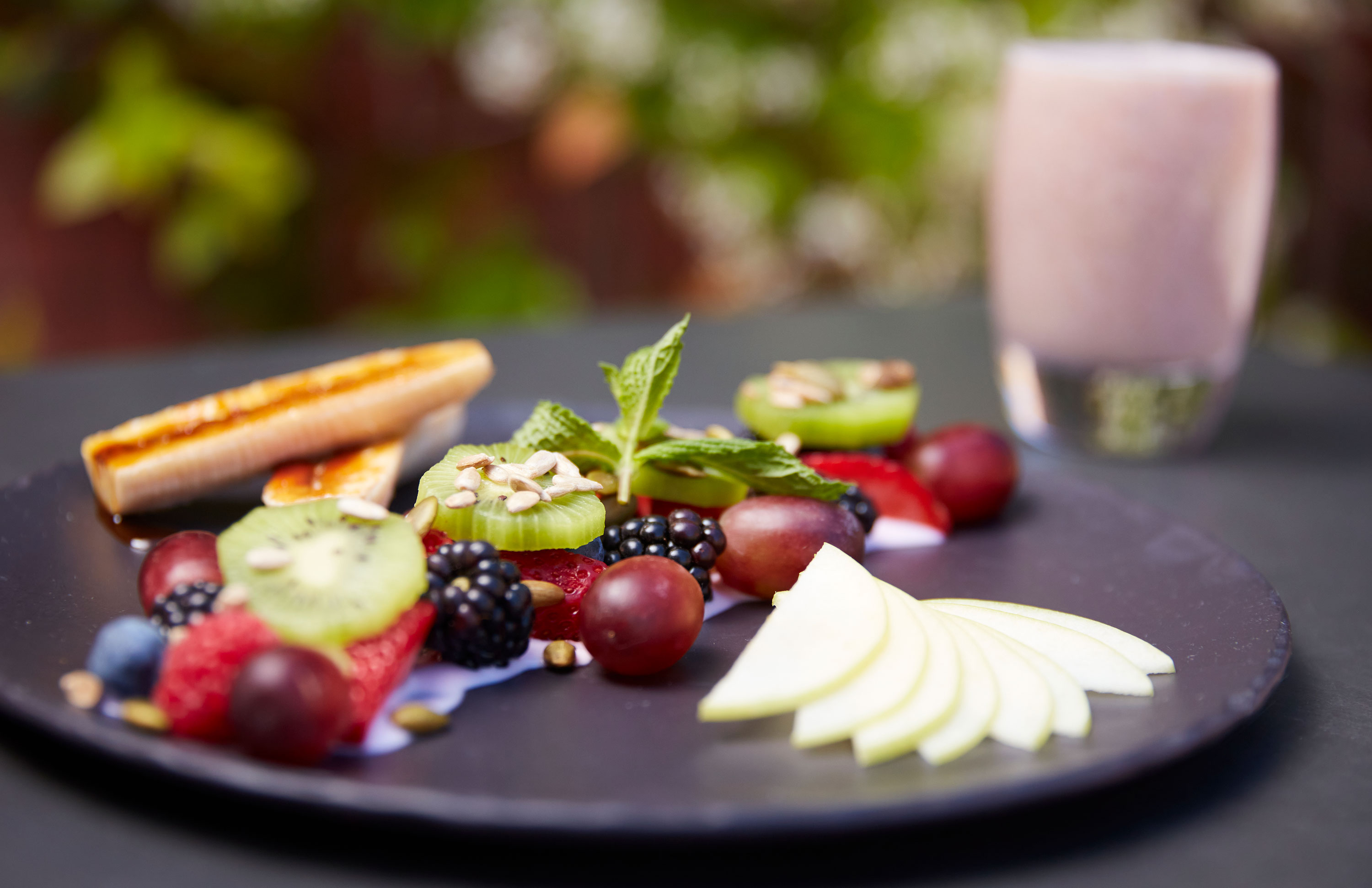a plate of fruit and a glass of pink smoothie
