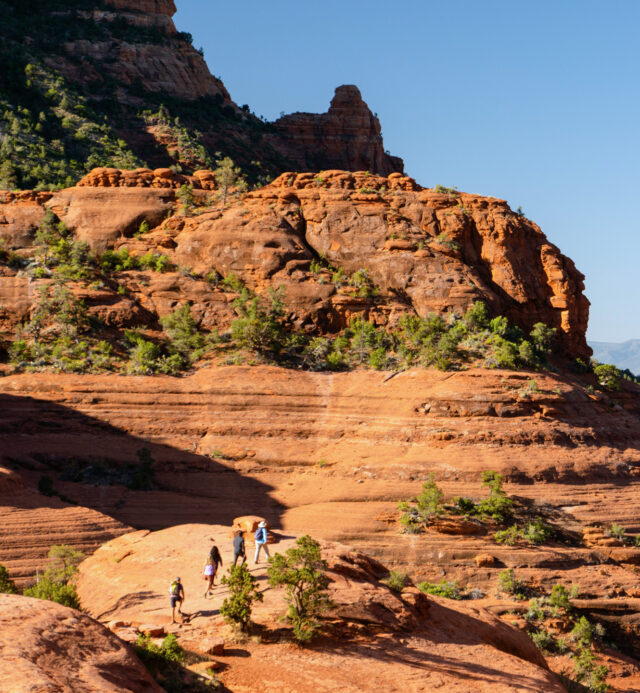 people hiking along trail with red rock formations