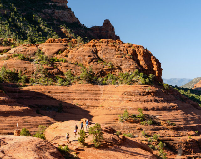 people hiking along trail with red rock formations