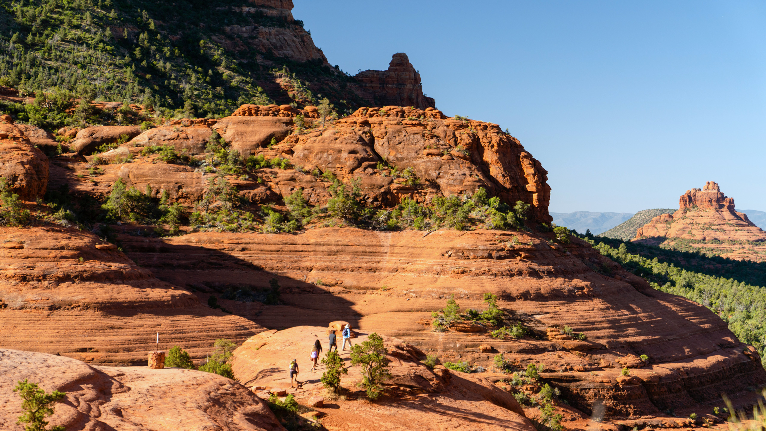 people hiking along trail with red rock formations