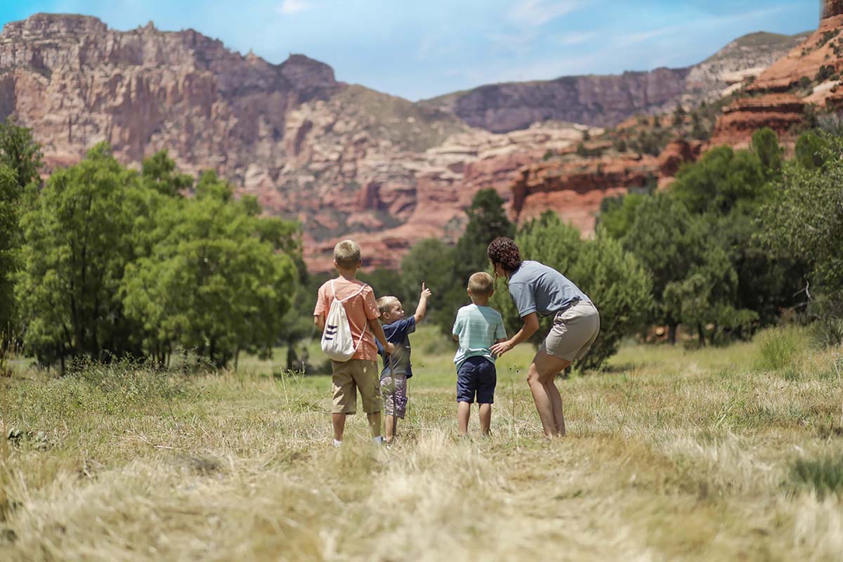 two kids and camp counselor in grassy field looking out at mountains