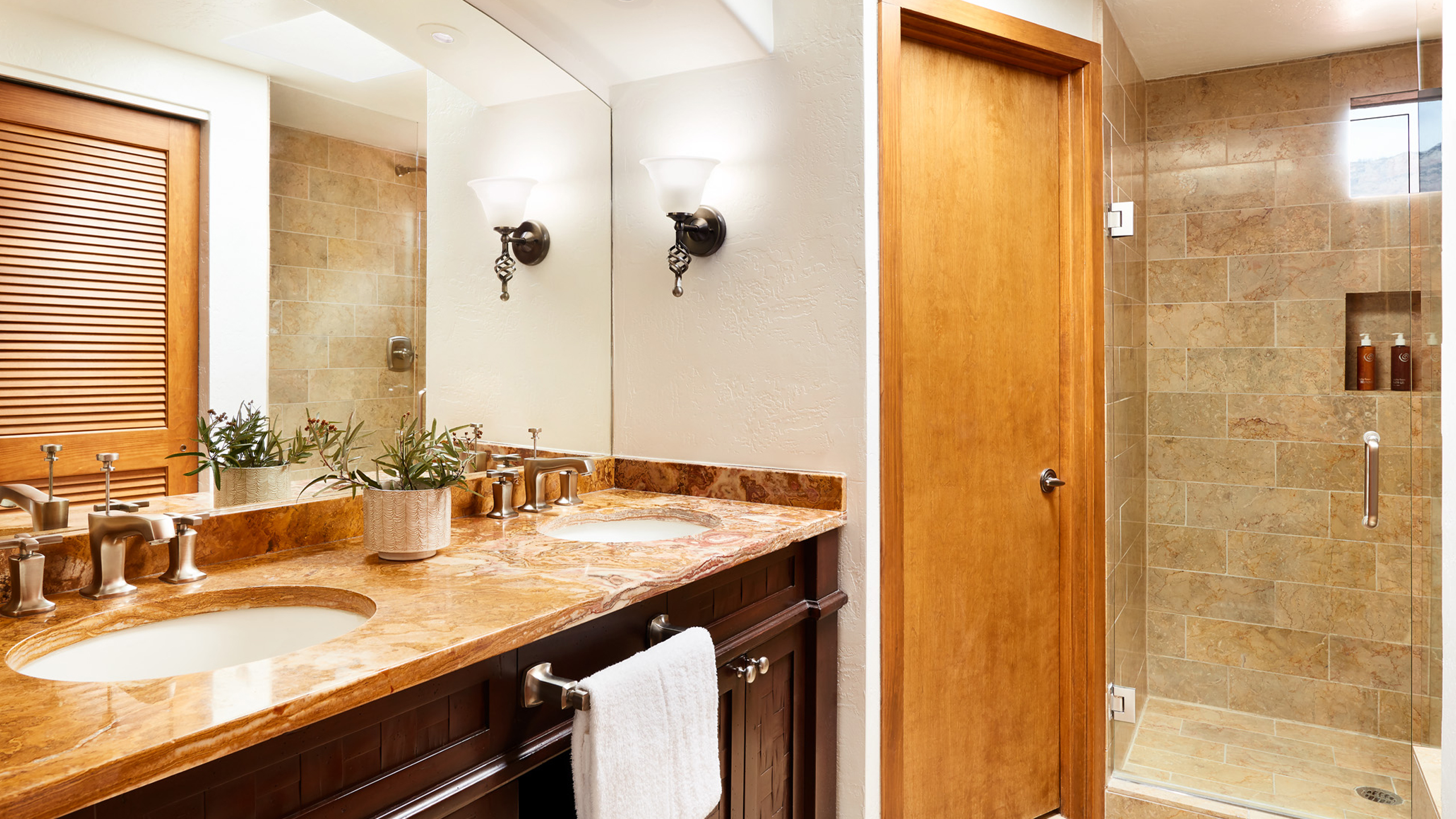 A bathroom with a double sink vanity, marble countertop, and tiled shower