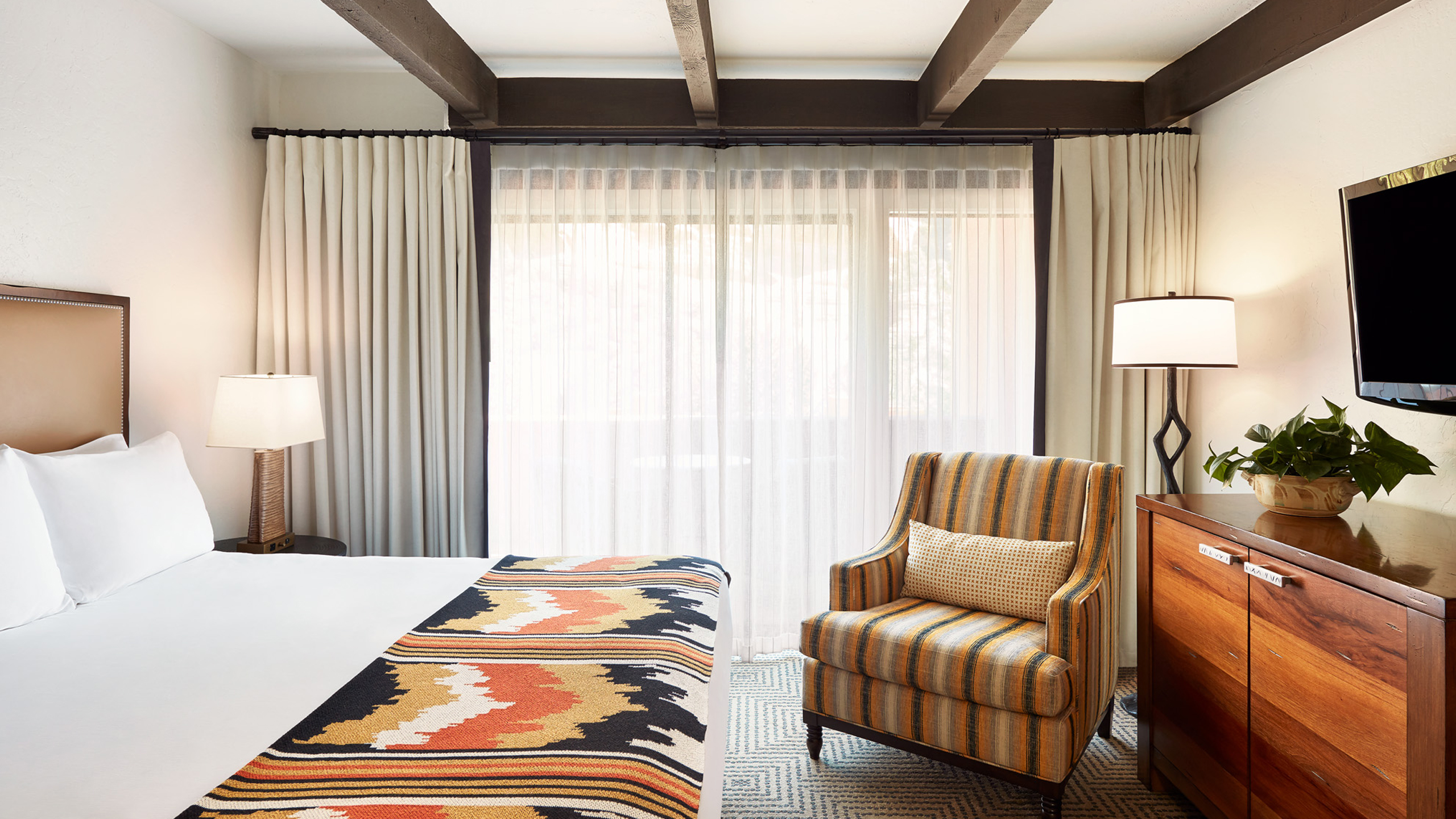 A hotel room with a bed, chair, TV, and dresser.