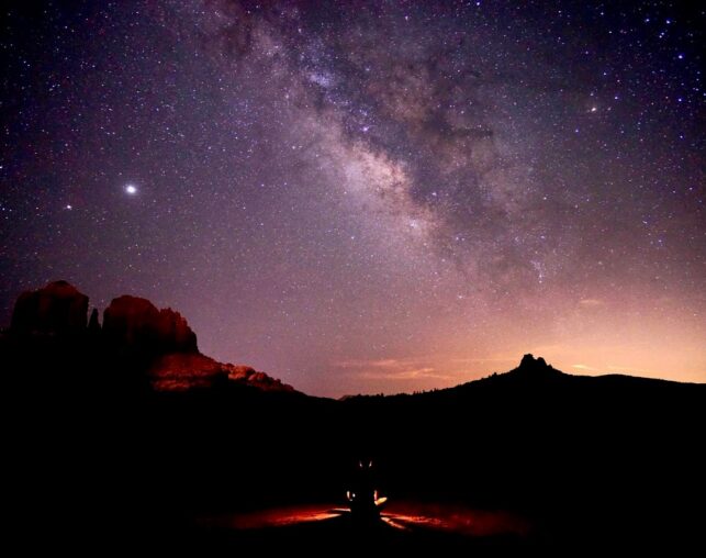 Person sitting on trail under dark, starry sky with Milky Way