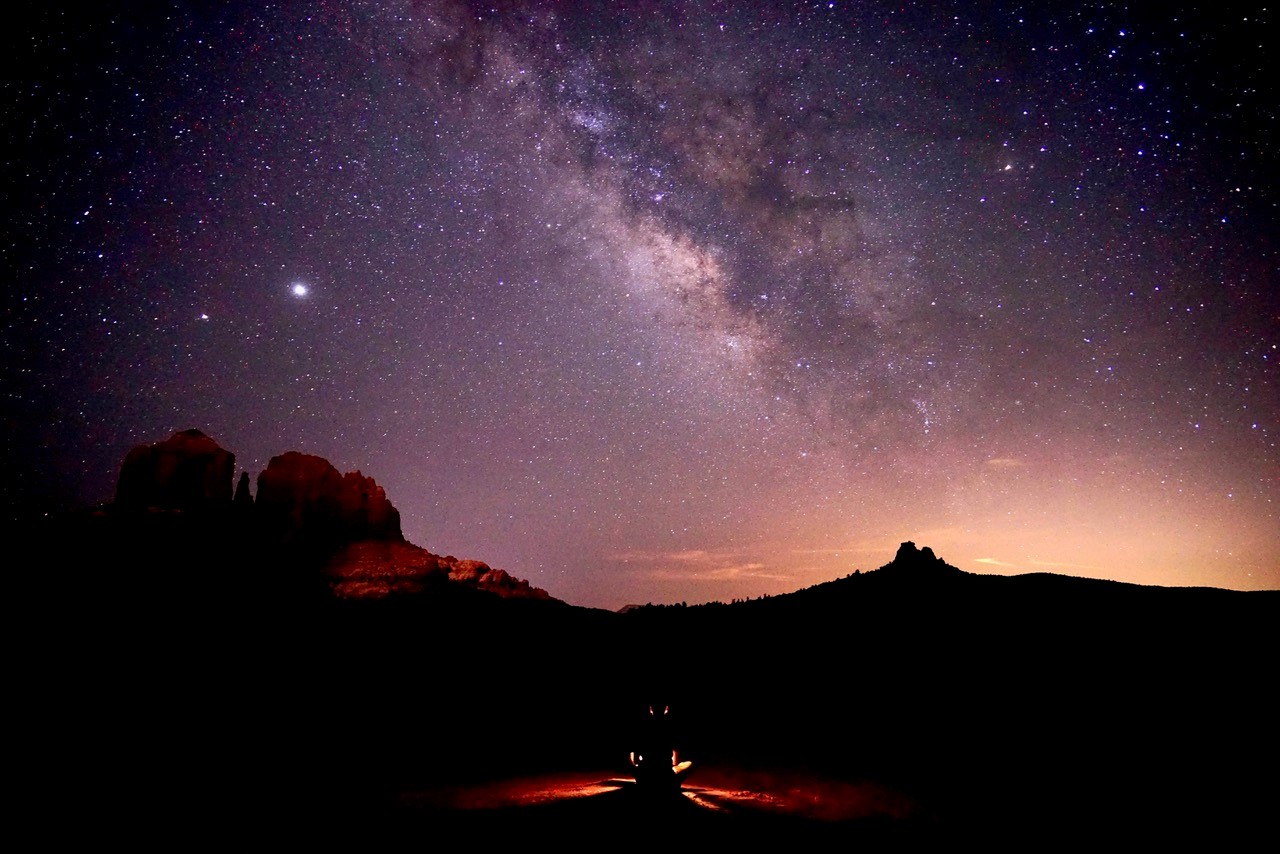 Person sitting on trail under dark, starry sky with Milky Way