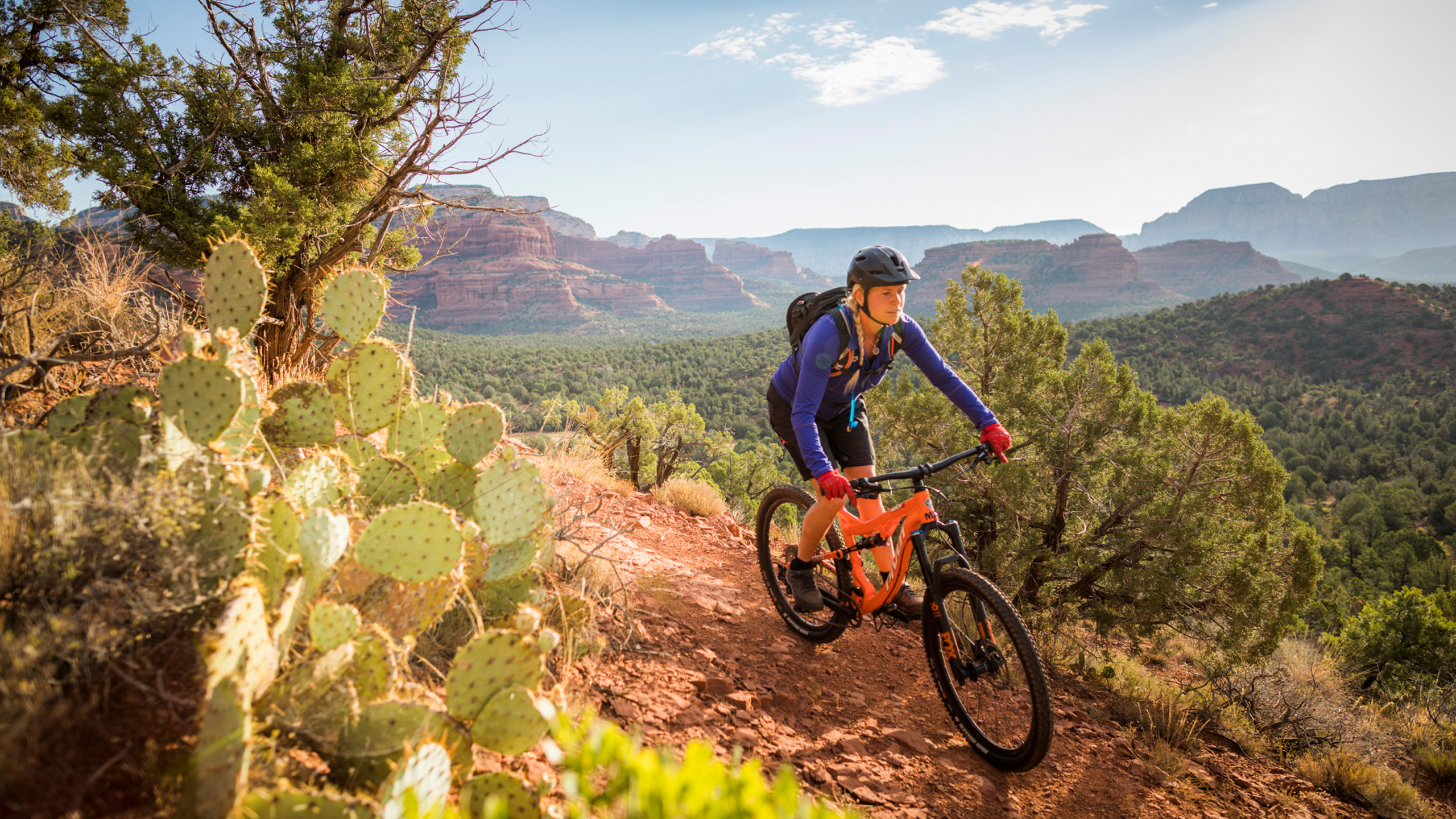 Woman on orange mountain bike with cactus on trail