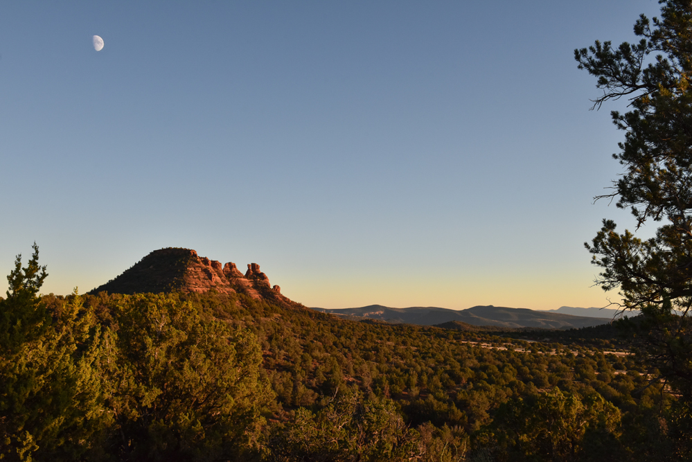 dusk scene with sun just below horizon and moon rising over mountain