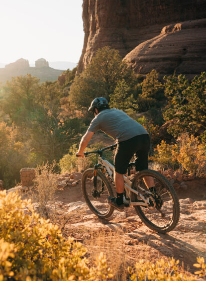man riding white bike on mountain bike trail with rock formations in the distance