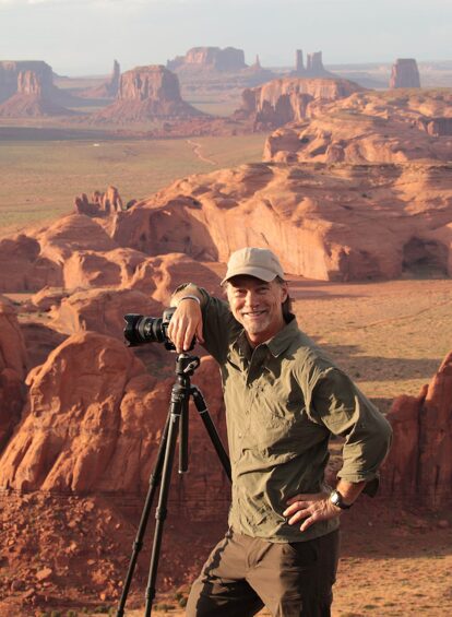 man leaning on camera tripod with desert landscape in background