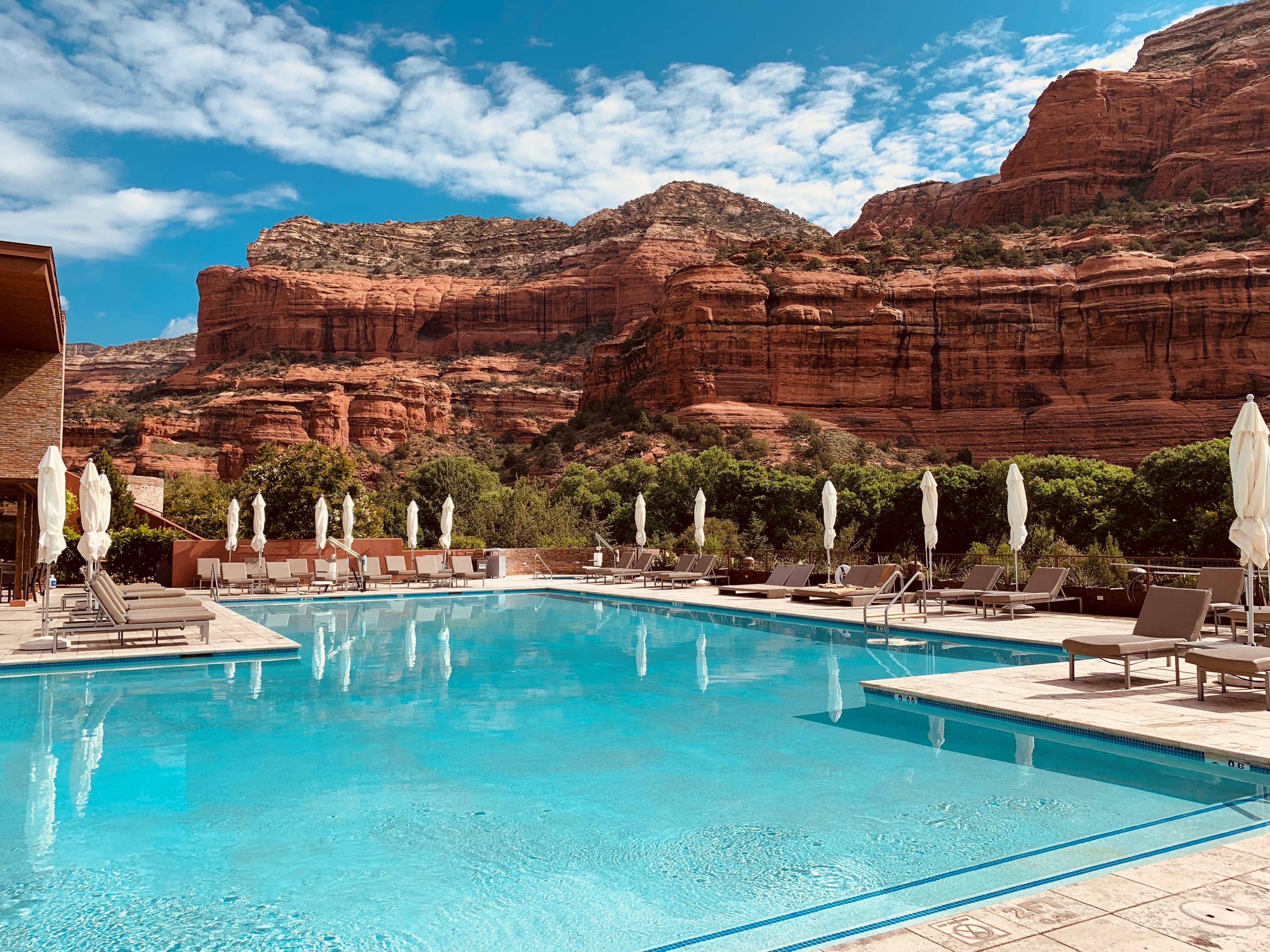 A large pool with lounge chairs and umbrellas in front of a mountain view.