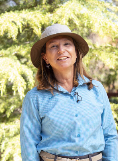 woman in blue shirt with brown shoulder length hair and hat