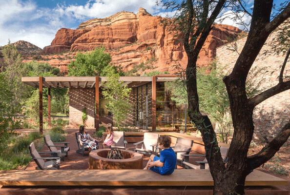 Child sitting on a wall next to a building with his mother and sister chatting by a fire pit nearby