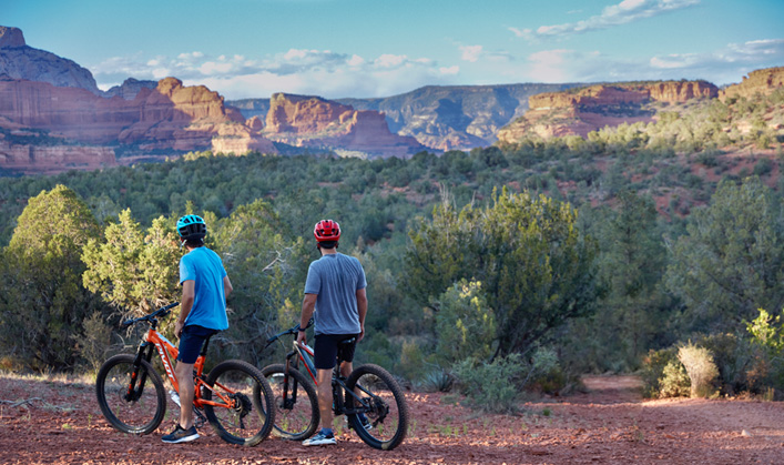 two mountain bikers in Sedona on trail looking out at red rock vista