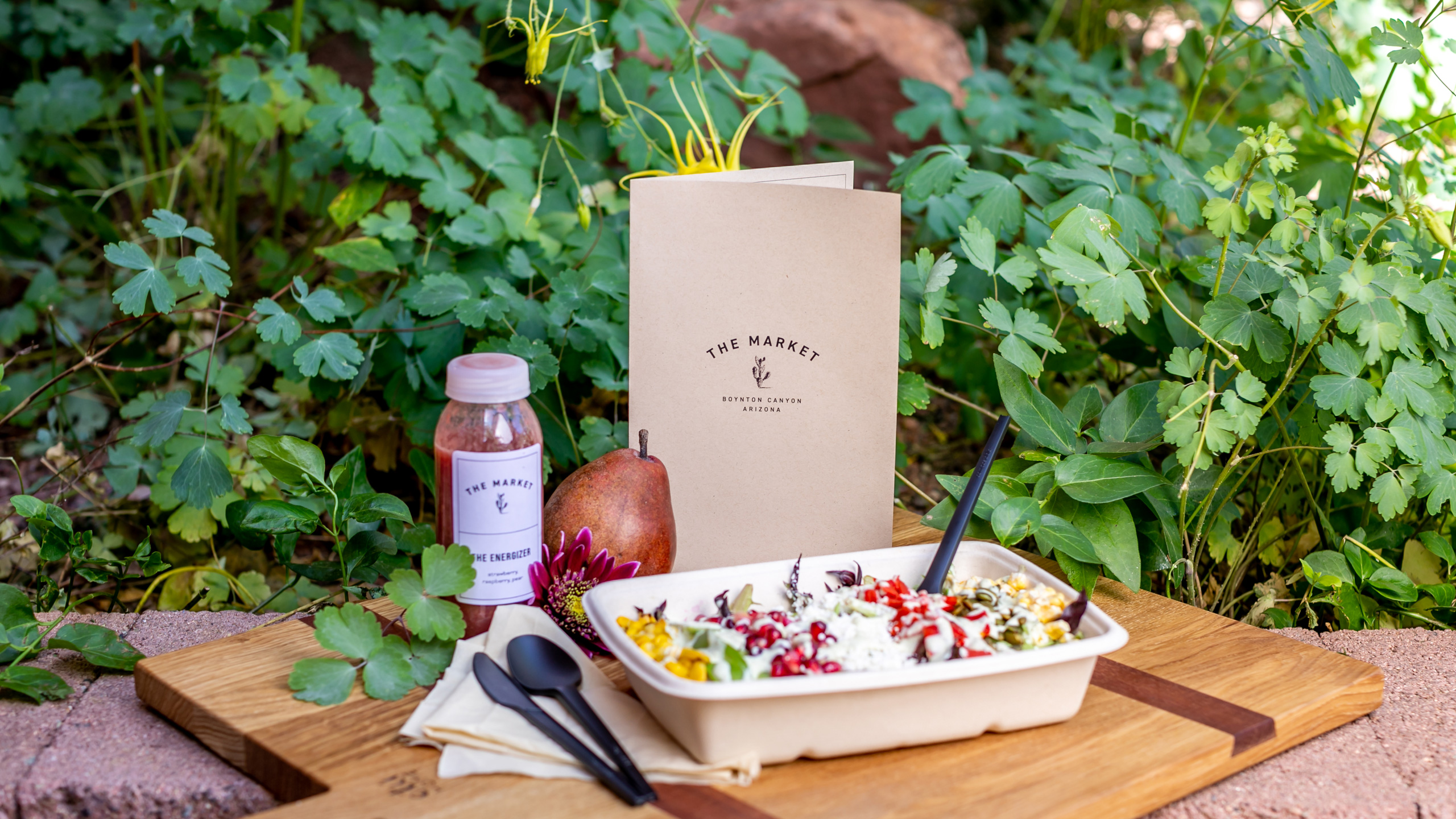 cutting board with pear, bottle of red juice, and bowl of salad