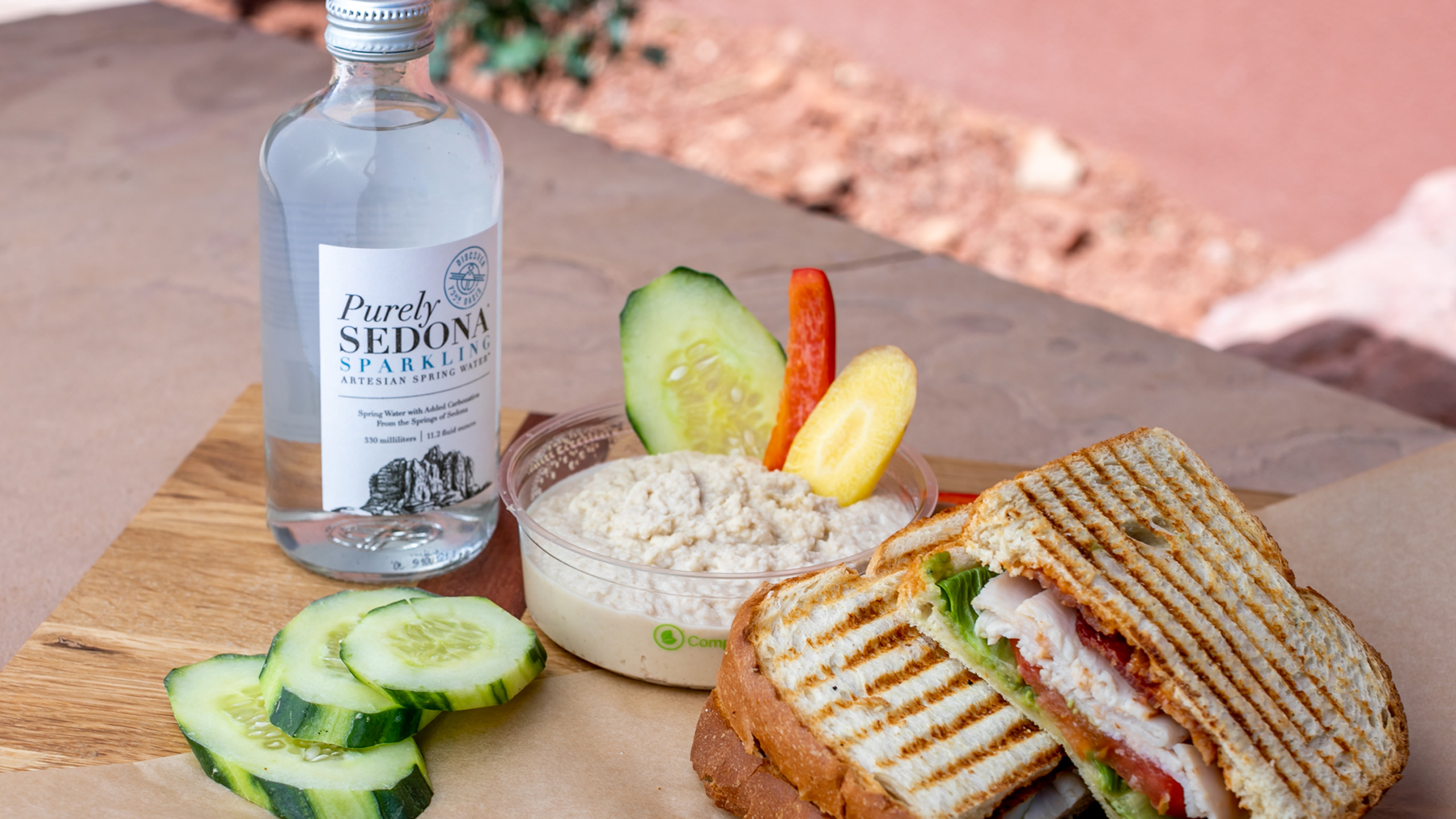 Bottle of sparkling water, hummus with veggies and toasted sandwich