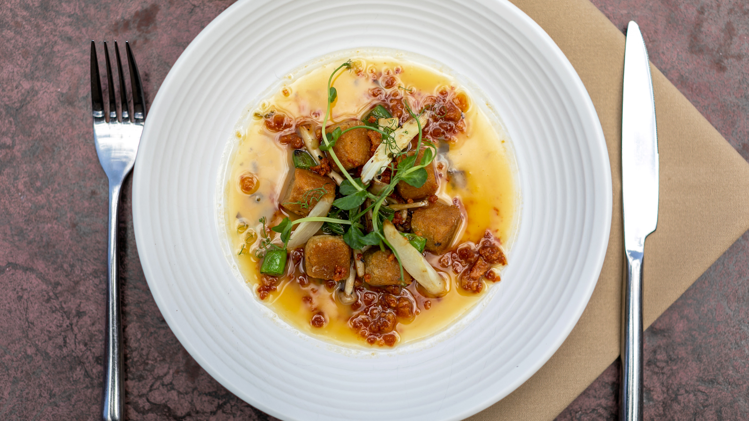 overhead view of mushroom gnocchi with greens, fork on left, knife on right