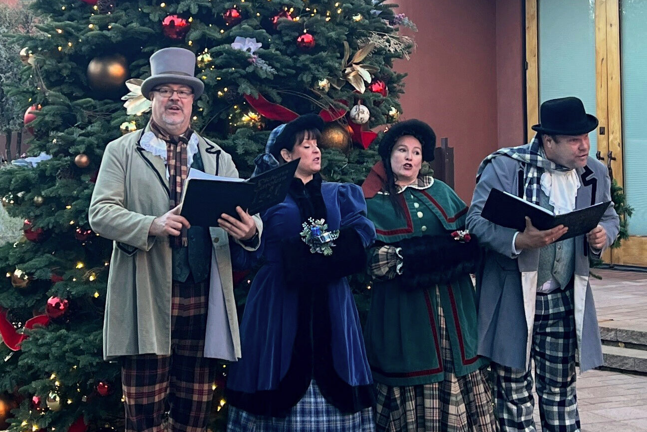 4 people caroling in traditional victorian costumes