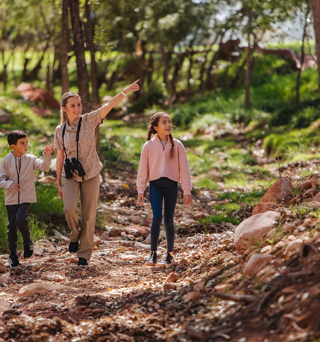 camp counselor with binoculars and kids walking in nature