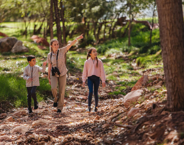 camp counselor with binoculars and kids walking in nature