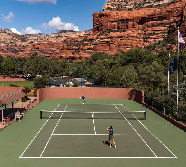two people playing tennis on courts surrounded by red rock formations