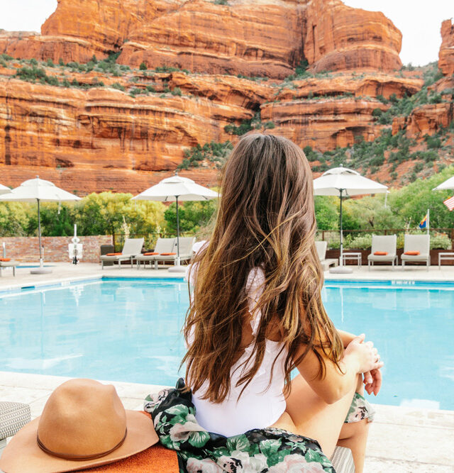 Woman in a white swimsuit by the side of the pool facing the red rocks of Sedona at our luxury Resort