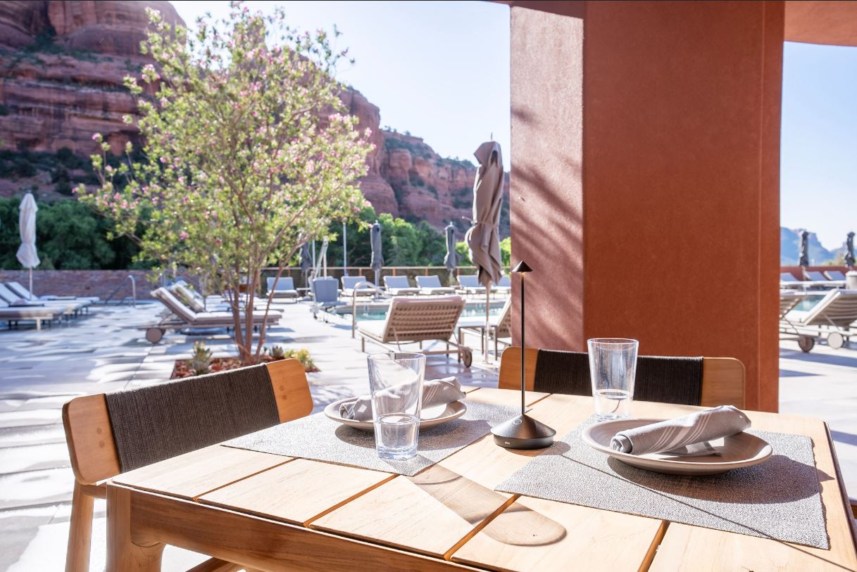 A table set for dining on an outdoor patio with a view of the pool and mountains.
